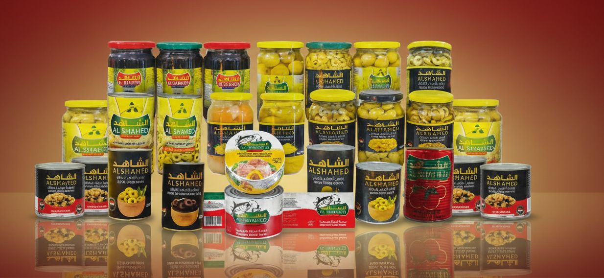 تشكيلة منتجات الشاهد: برطمانات زيتون بأغطية صفراء وخضراء وحمراء، وعلب تن ومعجون طماطم